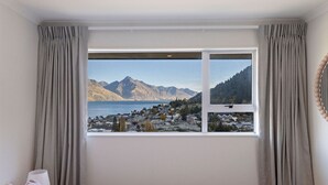 A bedroom with a large window offering a view of a mountainous landscape and a town. - Spectacular Views, Walk To Town, Freshly Renovated (Queenstown)