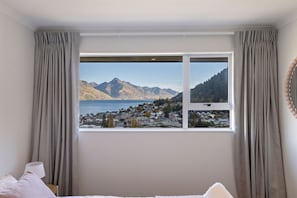 Un dormitorio con un ventanal que ofrece vistas a un paisaje montañoso y un pueblo.