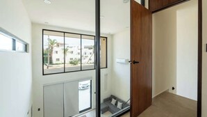 Ein modernes Interieur mit einer Schiebeglastür, Blick ins Freie, einem grauen Sofa und einer Holztür.