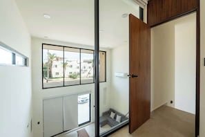 Ein modernes Interieur mit einer Schiebeglastür, Blick ins Freie, einem grauen Sofa und einer Holztür.