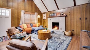 A cozy living room with a fireplace, wooden walls, a sofa, and a coffee table. - Cozy Cabin with Hot Tub, Game Room, Loft, Fire Pit (Pocono Lake)