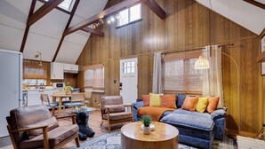 A loft-style living space with a high ceiling, wooden beams, a dining area, and a cozy seating area with a sofa and chairs. - Cozy Cabin with Hot Tub, Game Room, Loft, Fire Pit (Pocono Lake)