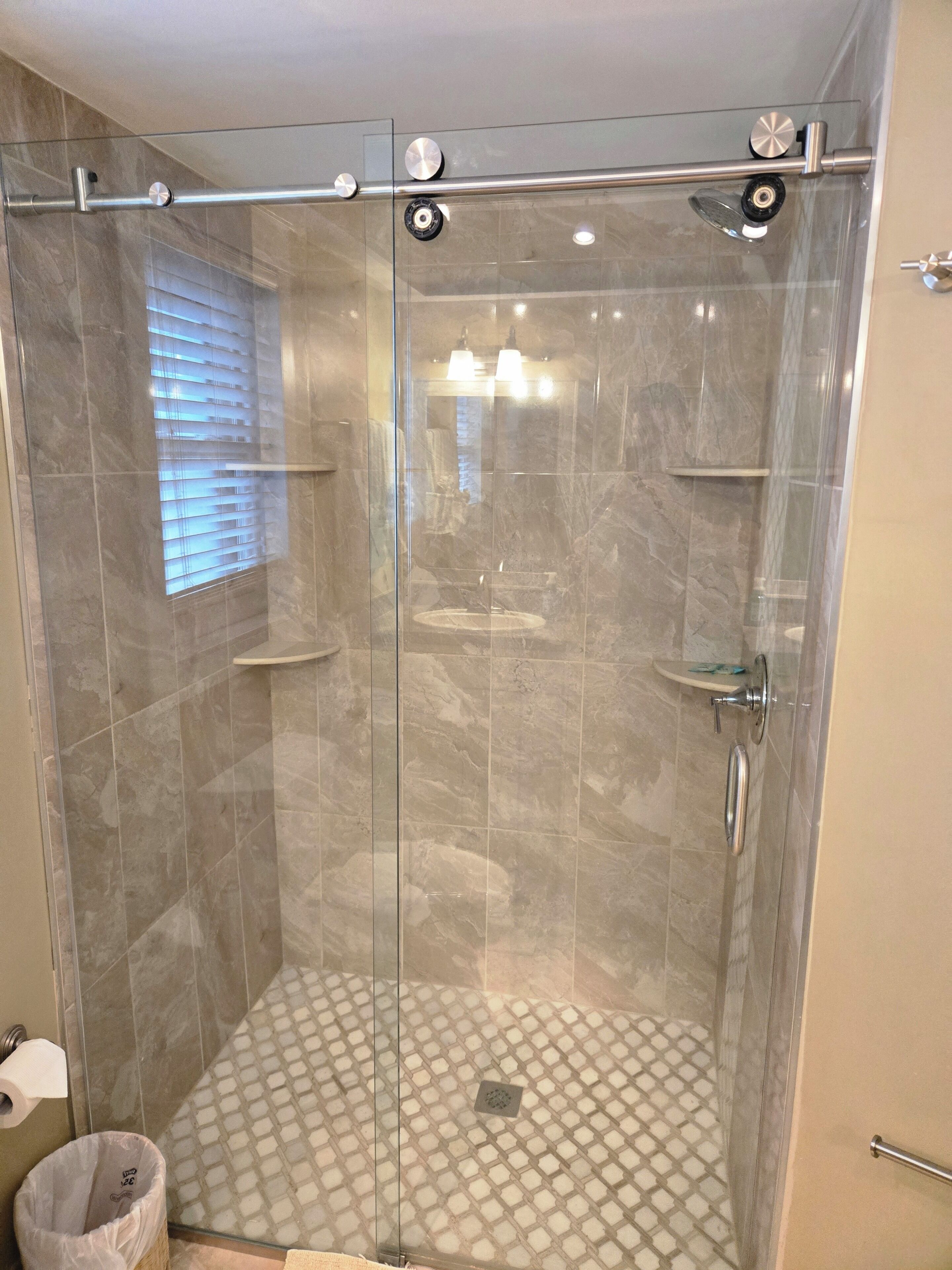 A walk-in shower with a glass door, a tiled floor, and a small window.