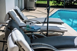Ein Liegebereich am Pool mit Liegestühlen, einem kleinen Tisch mit einem Glas und einem Pool im Hintergrund.