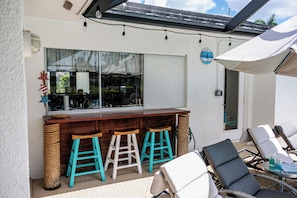 Eine Bar mit einer Holztresen, drei Barhocker und einem großen Sonnenschirm.