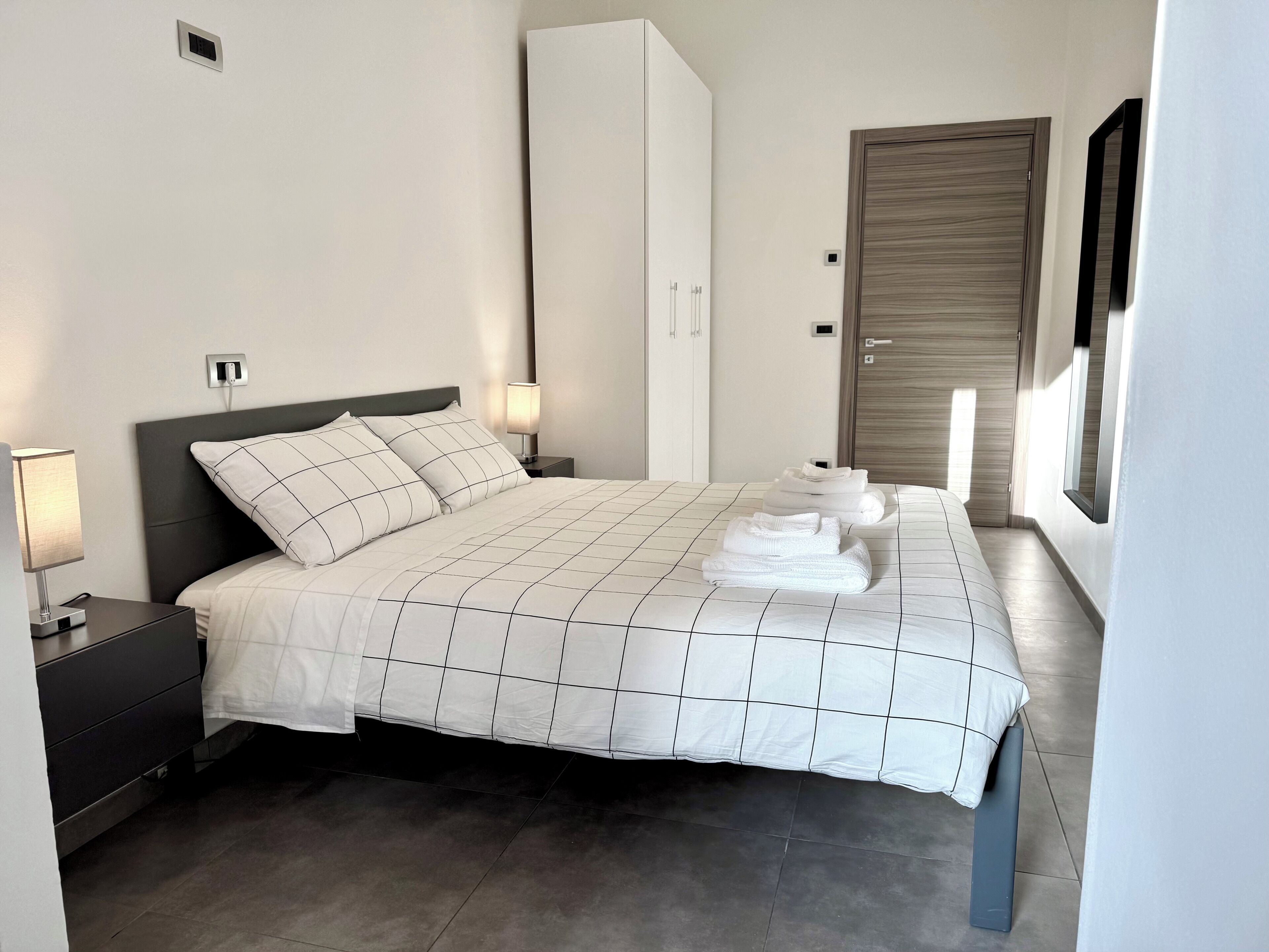 A neatly made bed with a white and black checkered bedspread, a bedside lamp, and a folded towel on the bed.