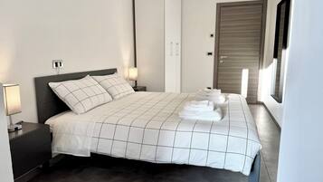 A neatly made bed with a white and black checkered bedspread, a bedside lamp, and a folded towel on the bed.