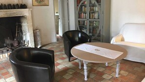 Una sala de estar con chimenea, una estantería, un sofá blanco y dos sillones negros.