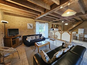 A rustic interior with exposed wooden beams, a sofa, a dining table, and a kitchen area. - The bird sanctuary (LUSIGNAN)