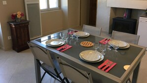 Una tavola imbandita per quattro, con piatti, bicchieri e posate, un vaso con fiori, e vista su una finestra e una porta.