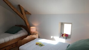 Una camera da letto con due letti, un comodino con una lampada, una piccola finestra con fiori e una trave in legno al soffitto.