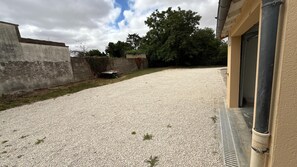 A gravel driveway leading to a building with a concrete wall and a metal door. - Le Gîte de Bré - Near Futuroscope (CHENECHE)