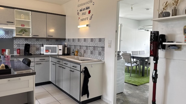 Uma cozinha moderna com micro-ondas, cafeteira e pia. Há uma área de refeições com mesa e cadeiras.
