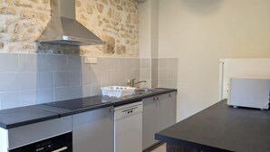 A modern kitchen with grey countertops, a dishwasher, a built-in oven, and a stone wall.