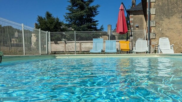 A clear swimming pool with a fenced area, lounge chairs, and a red umbrella.