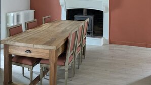 A dining room with a wooden table and chairs, a white fireplace, and a hanging light fixture.