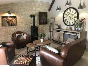 A cozy living room with leather furniture, a vintage clock, a fireplace, and a chessboard. - Domaine du Haut Vernay Scandinave (BOURNAND)
