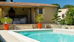 A swimming pool with a stone wall, outdoor furniture, and a covered patio area.