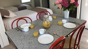 Een eettafel gedekt met borden, bekers en een karaf sinaasappelsap, met een bloevas op de achtergrond.