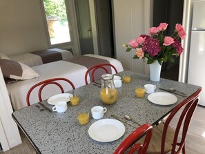 Ein Esstisch ist gedeckt mit Tellern, Tassen und einer Karaffe Orangensaft, im Hintergrund steht ein Blumenstrauß.