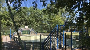 Een speeltuin met een klimrek, een basketbalveld en een omheind gebied met bomen.