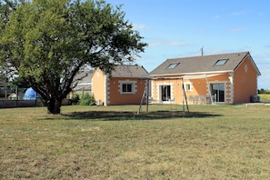 Ein Haus mit Veranda, Schaukel und einem großen Baum im Garten.