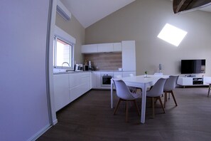 Una cocina moderna con armarios blancos, un comedor con mesa y sillas blancas, y un televisor de pantalla plana montado en la pared.