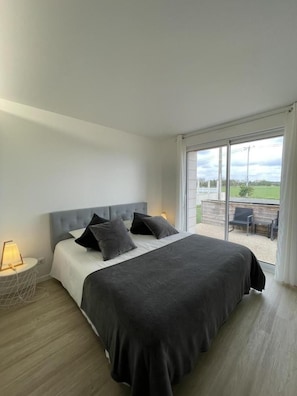 A bedroom with a large bed, a nightstand, a lamp, and a view of the outdoors through a sliding glass door. - Le Monteil - SAINT-JEAN-DE-SAUVES (SAINT-JEAN-DE-SAUVES)