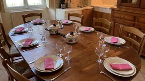 A dining room with a wooden table set for a meal, surrounded by chairs. - Le Petit Gîte du Theil Au Servant (LA CHAPELLE-VIVIERS)