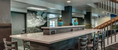 A modern bar area with a central island, bar stools, and a staircase leading to an upper level.
