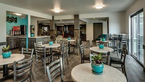 A modern dining area with round tables and chairs, potted plants, and a view of the kitchen area. - Comfort Inn & Suites Post Falls - Coeur Dalene West (Post Falls)