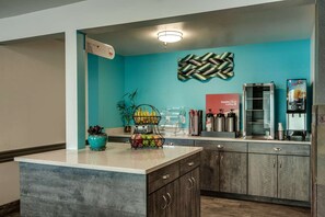 Un área de cocina con una isla central, una estación de café y un dispensador de jugo.