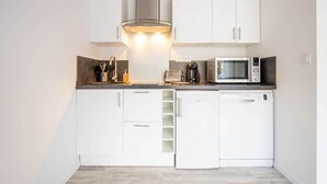 A compact kitchen with white cabinets, a stainless steel range hood, a microwave, a coffee maker, and a dishwasher. - Le Gite du Marronnier (MONTAMISE)