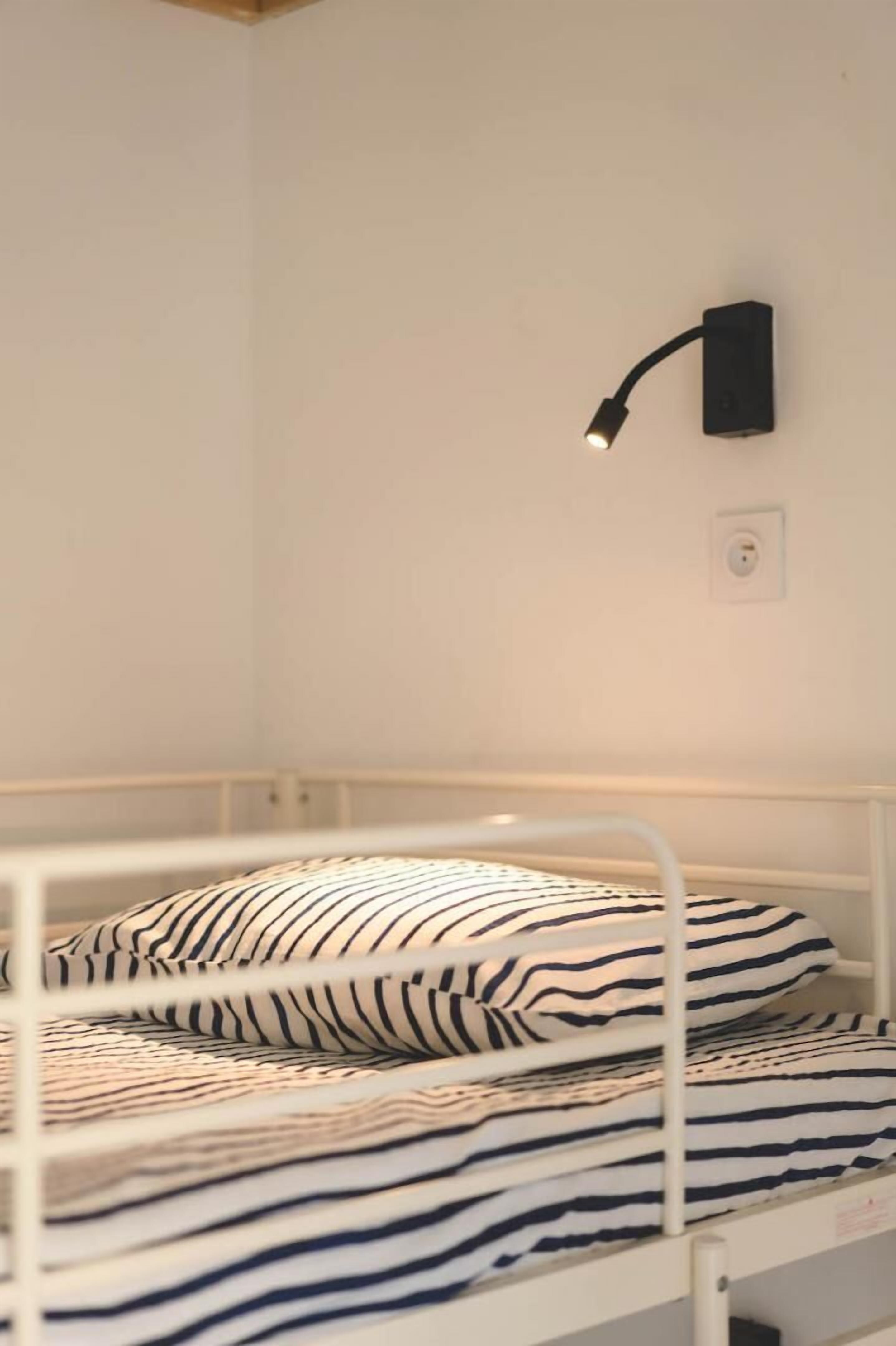 Una cama individual con ropa de cama a rayas, una lámpara de lectura fijada a la pared y un enchufe.