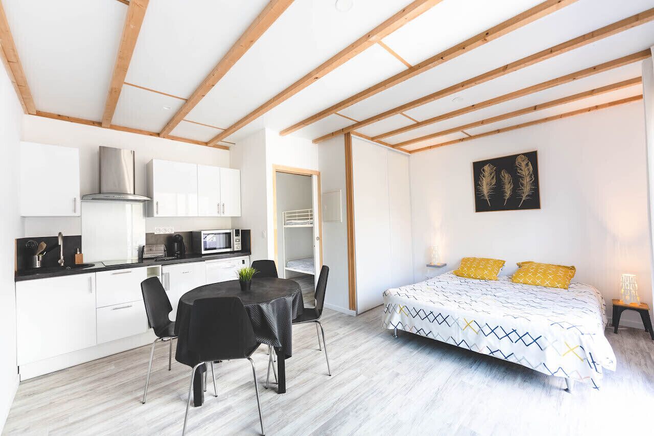 Een moderne keuken met witte kastjes, een eettafel met stoelen, een bed met beddengoed met een patroon, en een schilderij aan de muur.