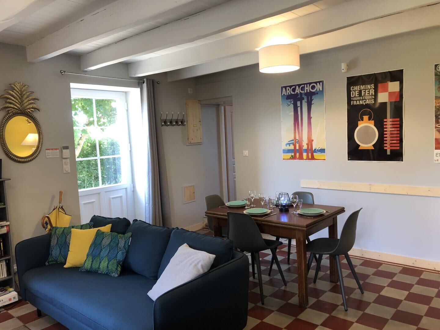En stue med sofa, spisebord med stole, et spejl og et vindue med gardiner.