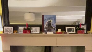 En pejs med en bog med titlen 'Illustration' på pejsen, en lampe og indrammede billeder.
