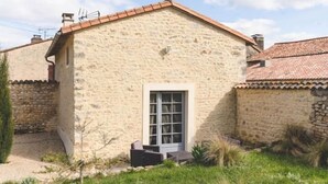 A stone building with a tiled roof, a door, and a small garden area with grass and plants. - Le Gite du Puits - MONTAMISE (MONTAMISE)