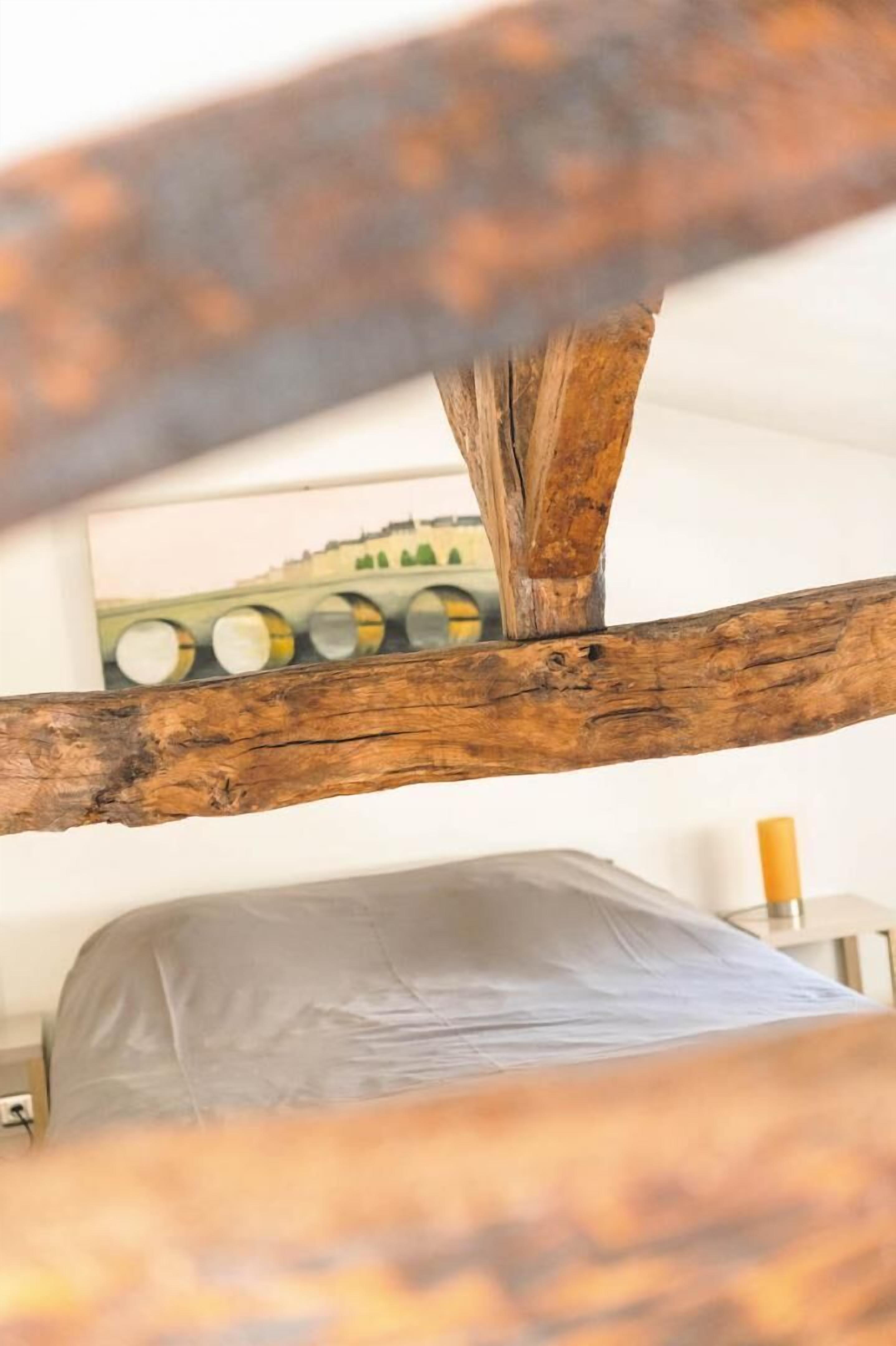 Une structure en poutres de bois dans une pièce où se trouvent un lit et un tableau accroché au mur.