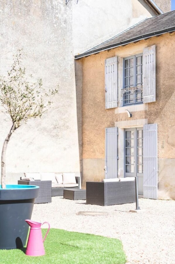 A building with a stone facade, a tree, outdoor furniture, and a large planter. - Le Gite du Manoir - MONTAMISE (MONTAMISE)