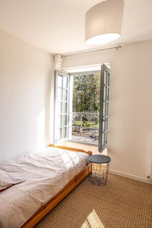 A bedroom with a bed, a small round table, a window with an open view to an outdoor area. - Le Gite du Manoir - MONTAMISE (MONTAMISE)