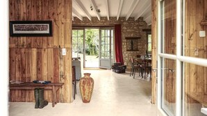 Un interior de madera con una pared de piedra, un jarrón grande y un comedor visible a través de un vidrio.
