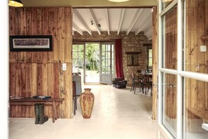Un intérieur en bois avec un mur en pierre, un grand vase et un coin repas visible à travers une porte en verre.