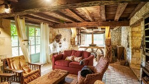 Un interior rústico con vigas de madera a la vista, un sofá rojo, sillones estampados y una pared de piedra.