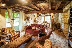 Un intérieur rustique avec des poutres apparentes, un canapé rouge, des fauteuils à motifs et un mur en pierre.