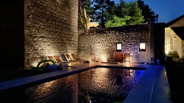 Un espacio al aire libre con paredes de piedra, piscina, asientos e iluminación ambiental.