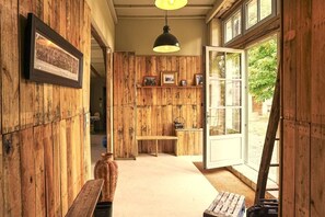 A wooden interior with a bench, a hanging light fixture, and a door leading outside. - The Gaudais mill (OYRE)