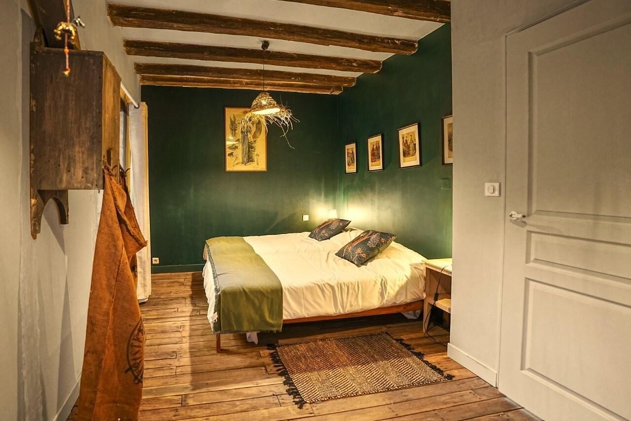 Ett rum med en säng, synliga träbjälkar, en hängande lampa och inramade tavlor på väggen.