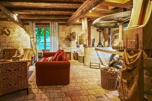 A rustic interior with stone walls, a wooden ceiling, a red sofa, and a stone fireplace. - The Gaudais mill (OYRE)