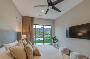 Ein Schlafzimmer mit Bett, Deckenventilator, Fernseher und Blick auf eine angelegte Grünfläche.